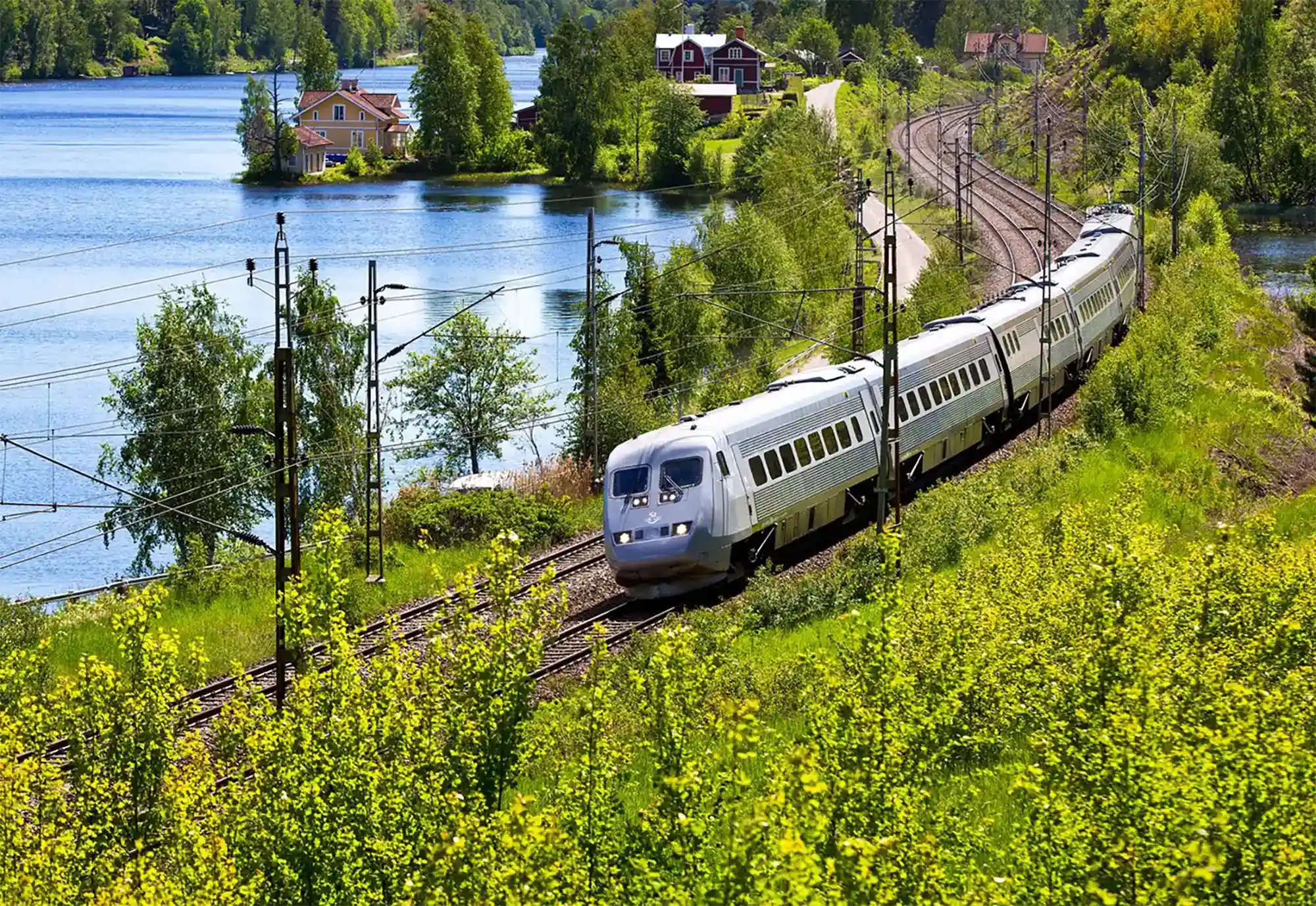 Ein Zug fährt durch die schwedische Landschaft, an einem See entlang