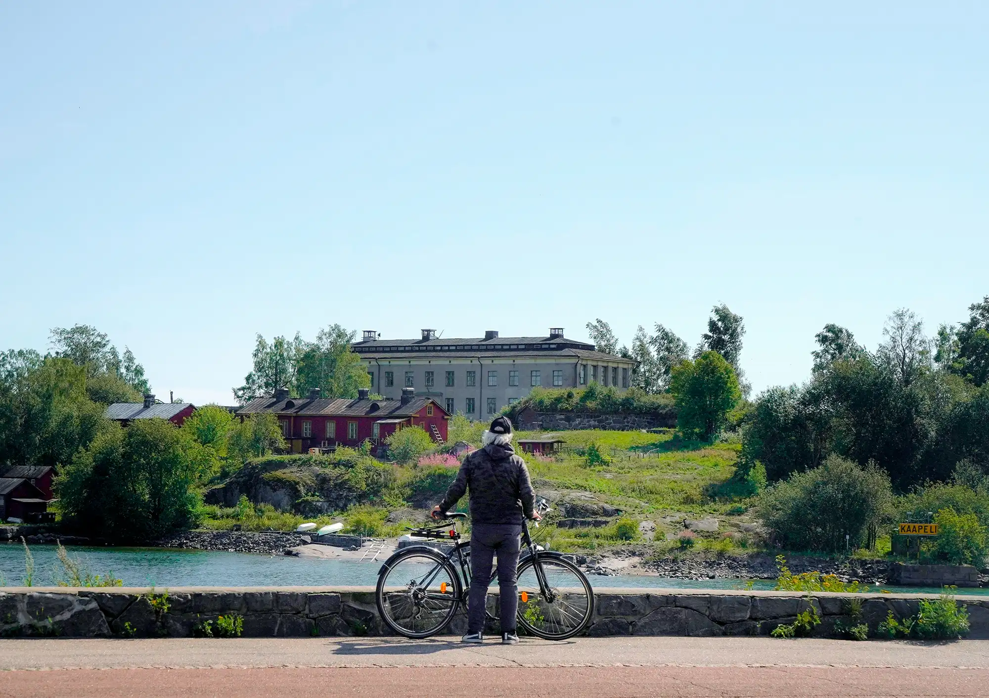 Ein Radfahrer schaut über das Wasser zur Insel Harakka (Harakansaari) südlich des Stadtzentrums von Helsinki, Finnland