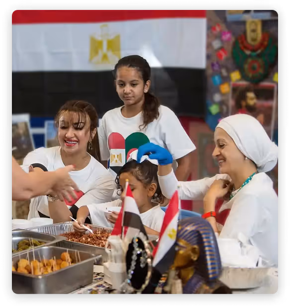 Families serving food at an Egyptian-themed booth during a school international cultural fair