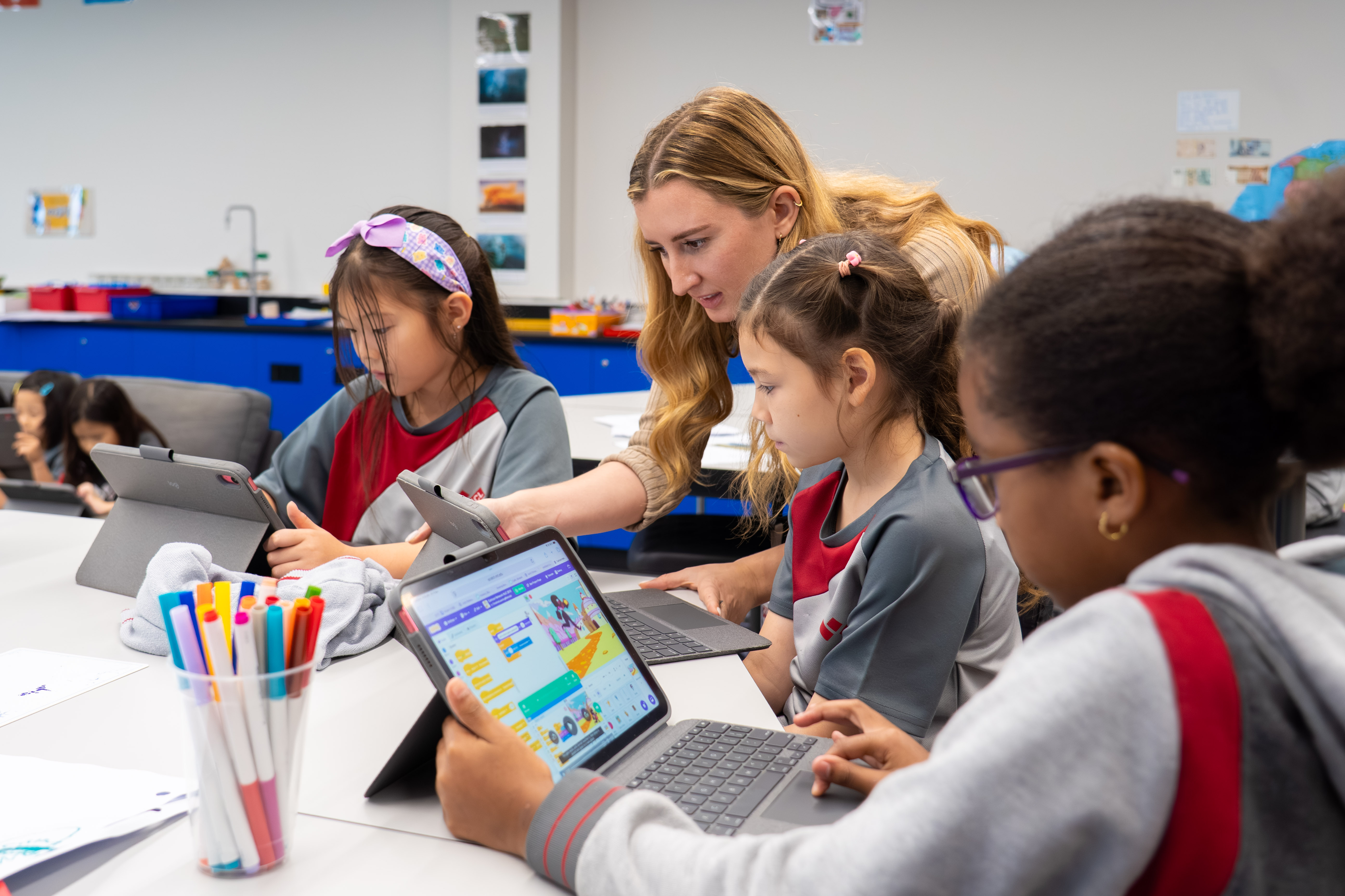 Teacher assisting young students using tablets during a technology class