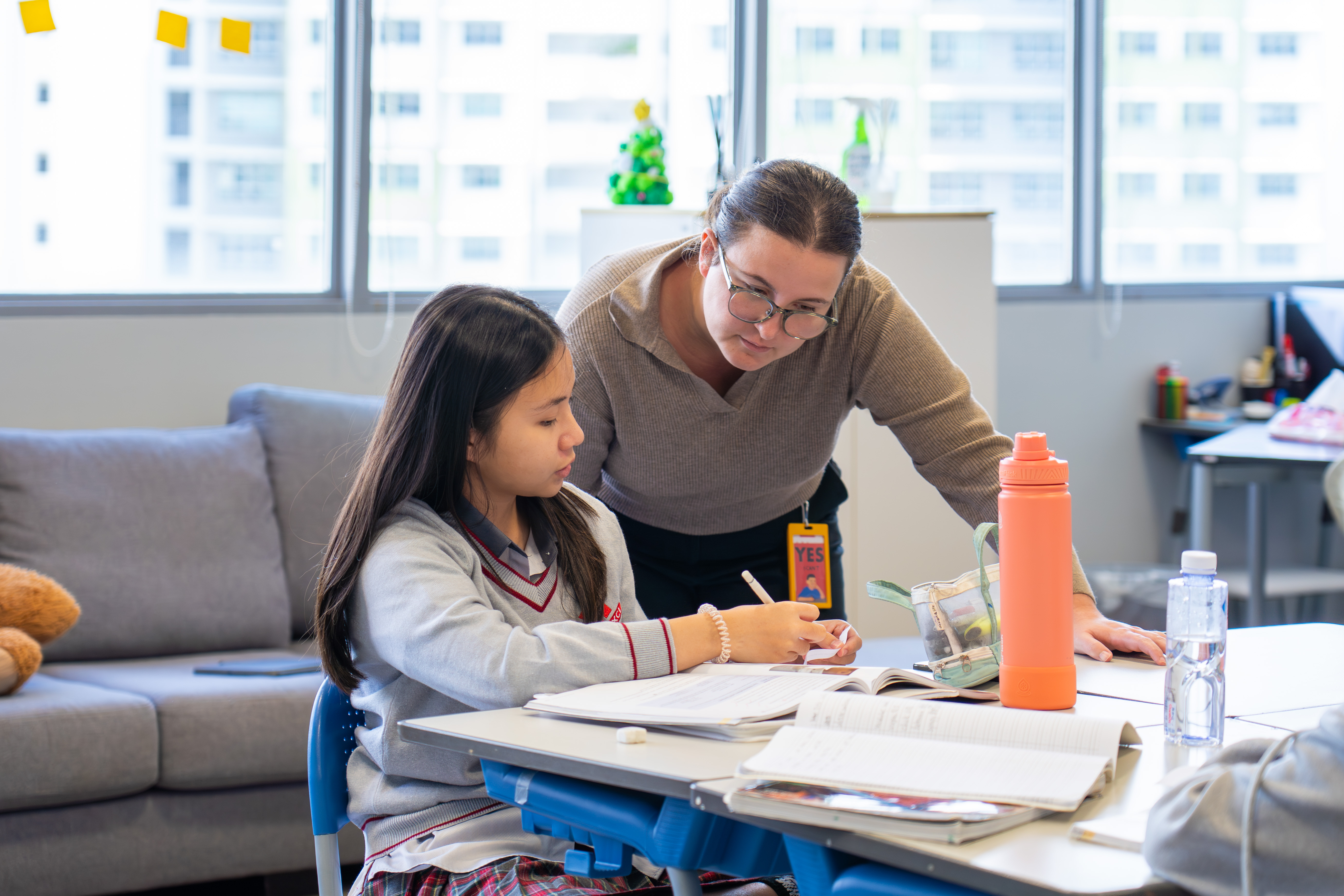 Teacher leaning over to help a student with written work at her desk