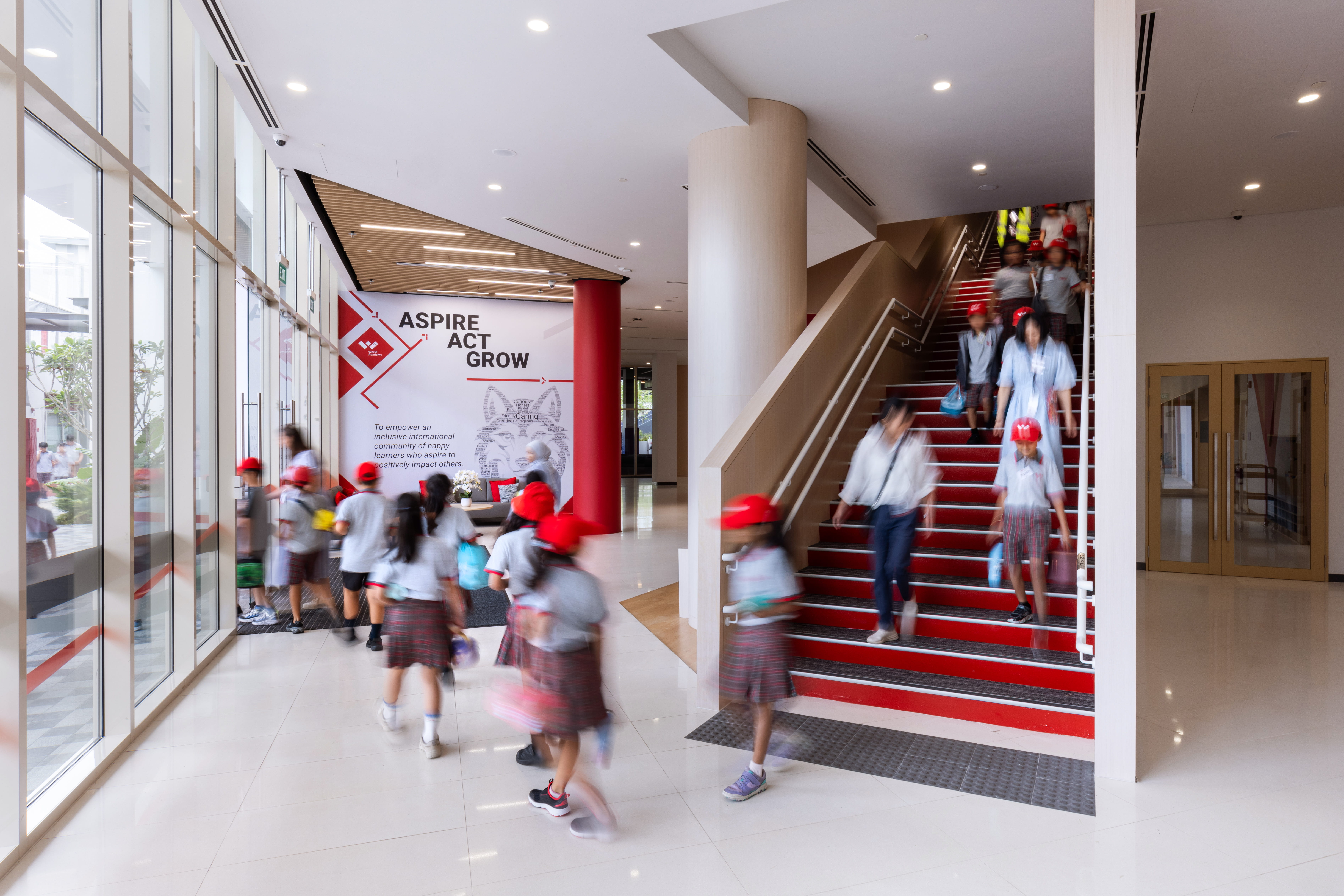 Students walking through XCL World Academy's main lobby past an Aspire Act Grow banner