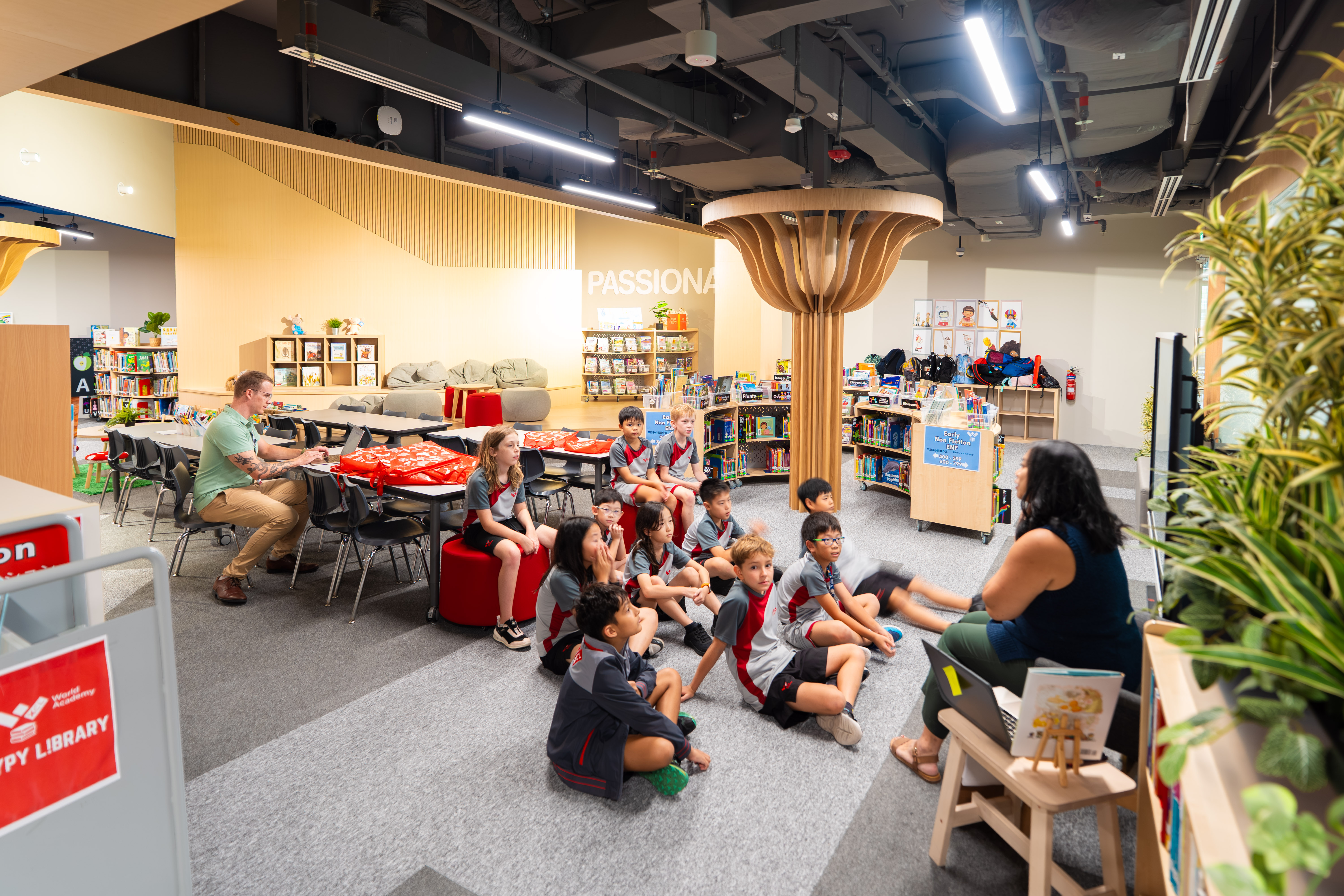 Primary students seated on the floor listening to a teacher read in the school library