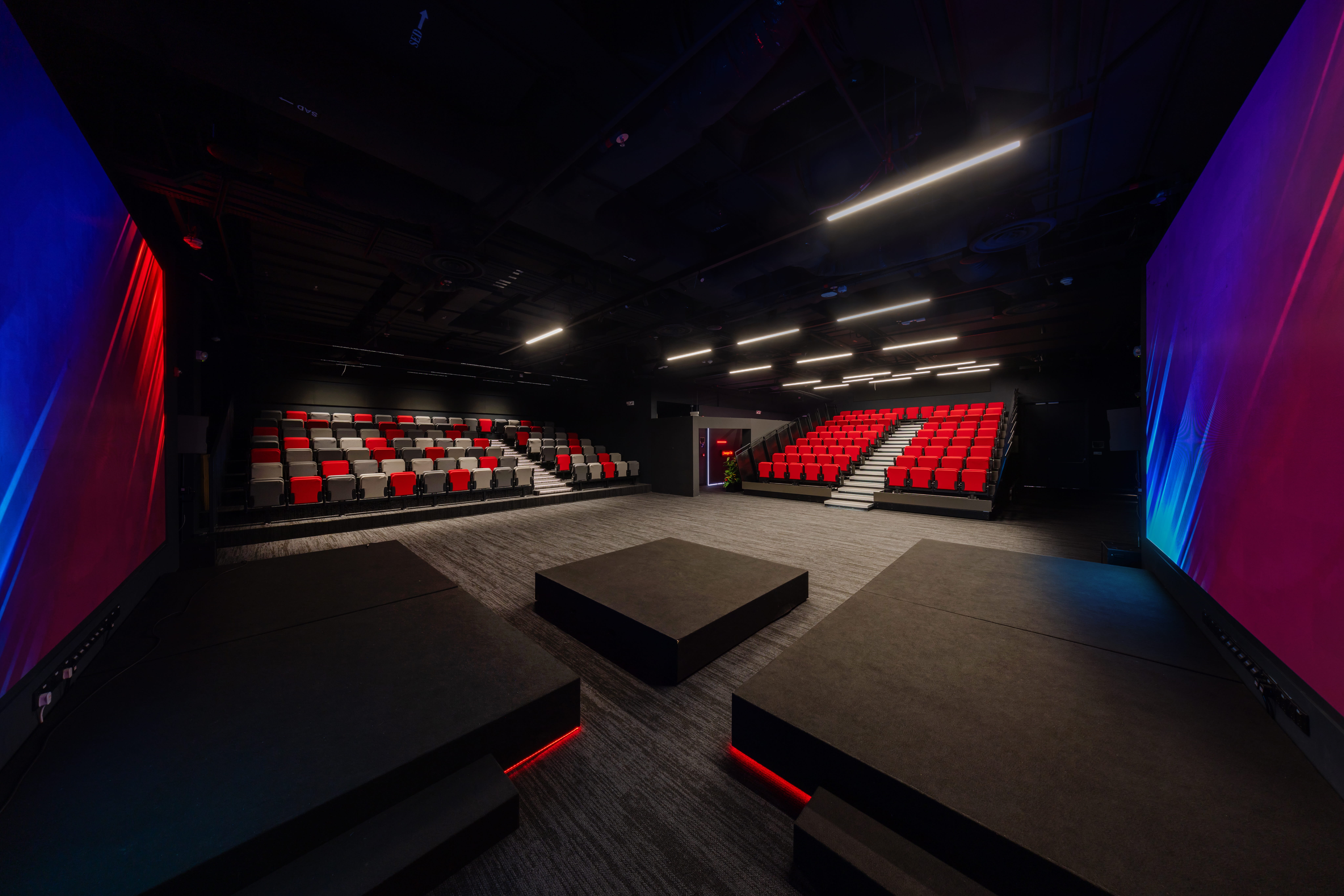 Empty school black-box theatre with tiered red seating and stage lighting