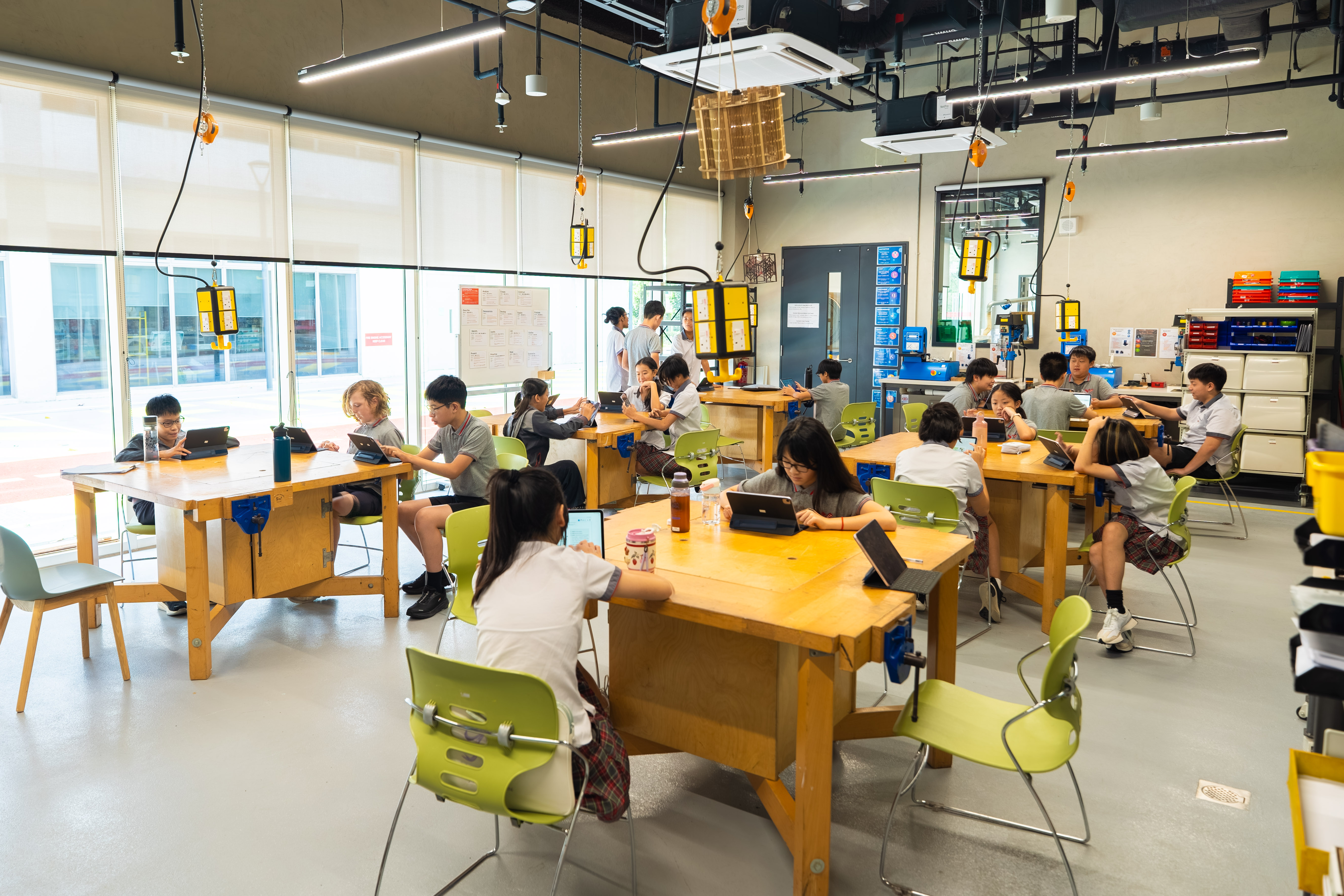 Students working on tablets at wooden workshop tables in a makerspace classroom