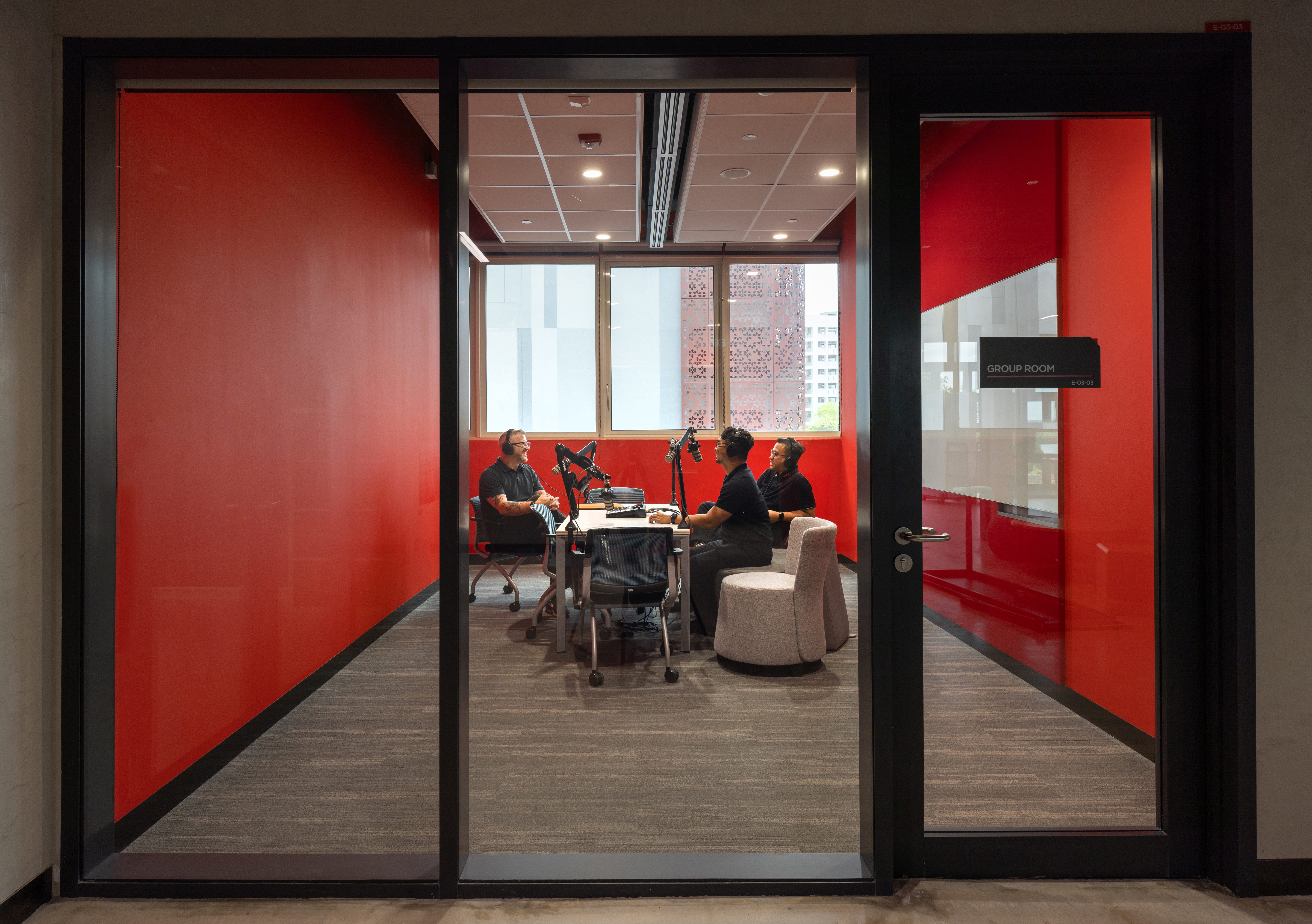 Three students in a recording studio with microphones and red glass walls