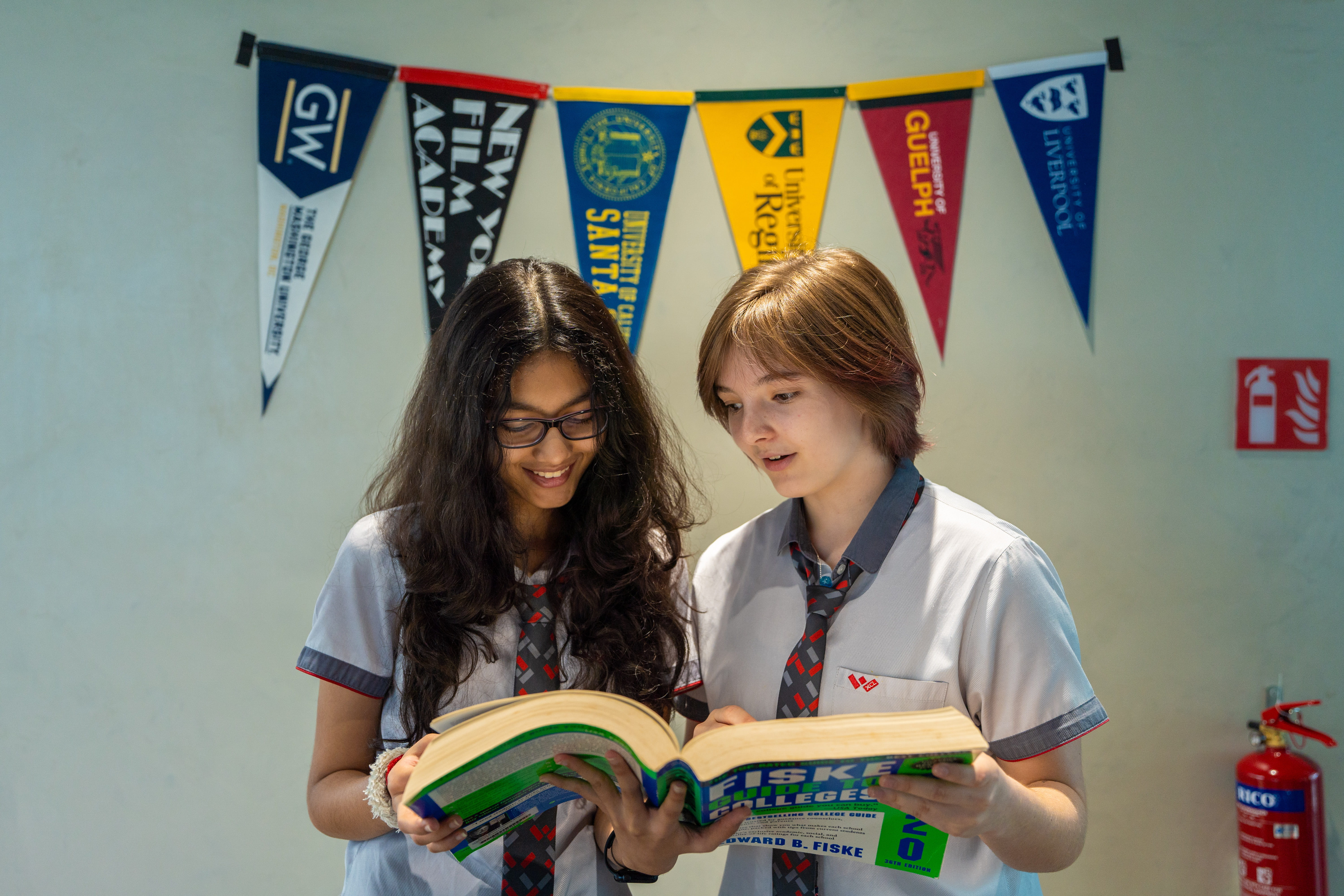 Two students reading a college guide beneath university pennants
