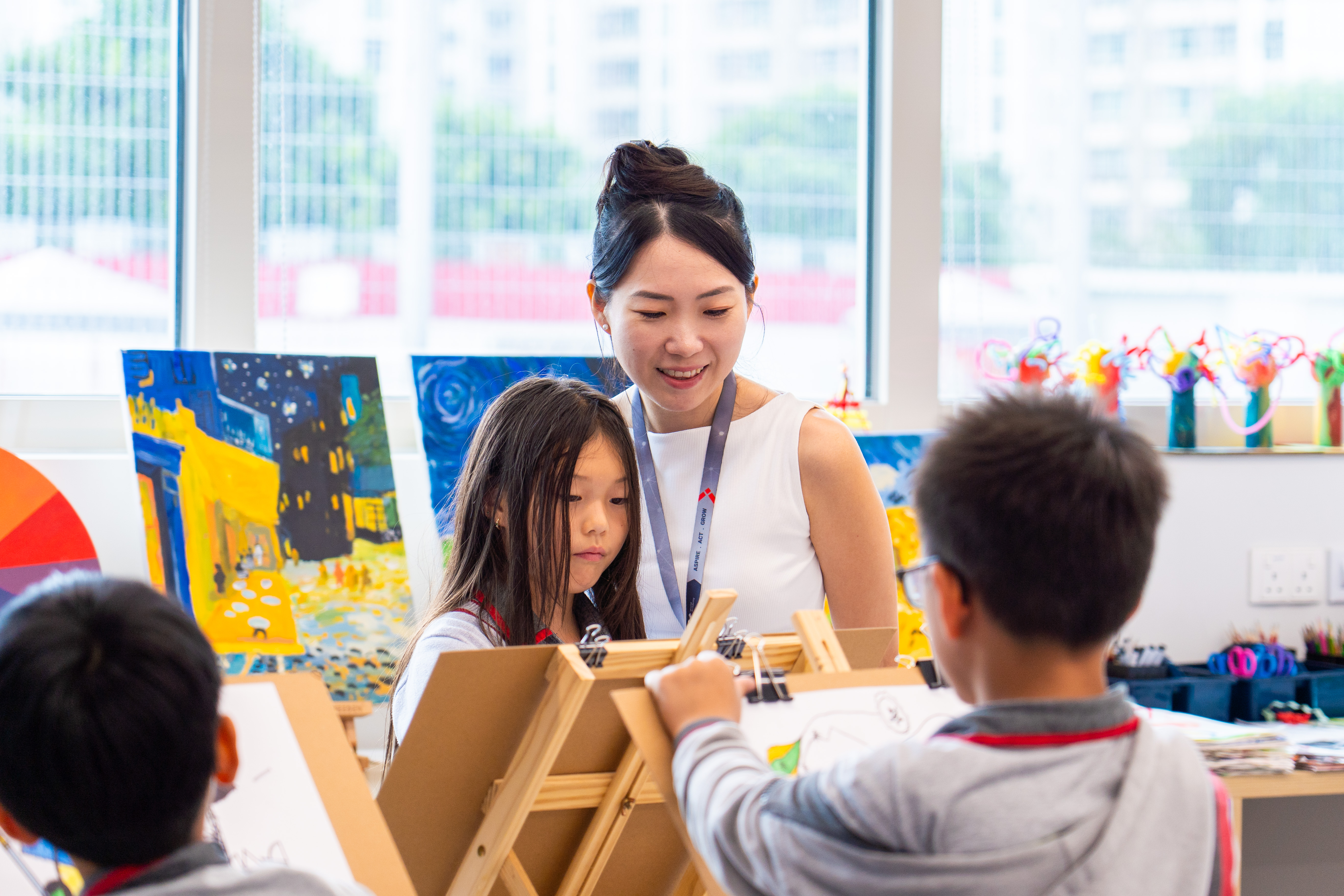 A teacher guiding young children painting at easels