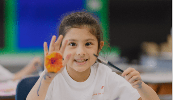 A smiling young student showing a paint-covered hand in art class