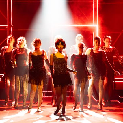 Students performing a dance number in black costumes under red stage lighting