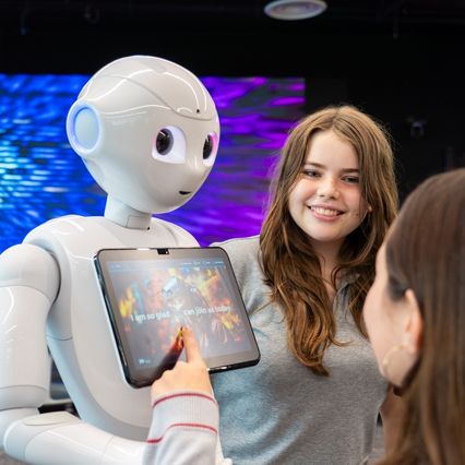 A student smiling at a white humanoid robot during an AI lesson