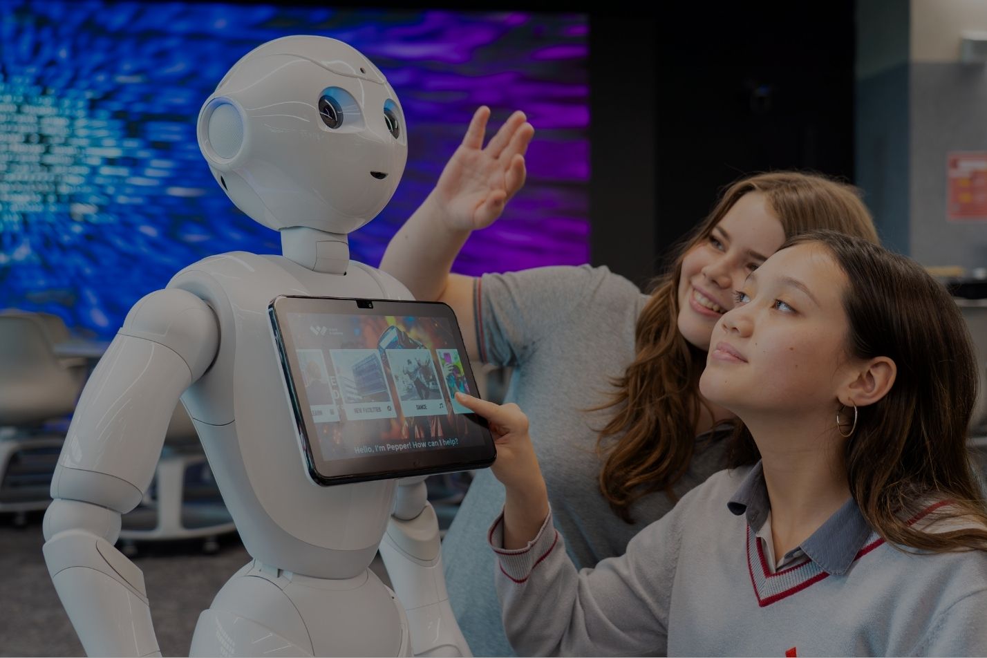 Two students interacting with a white humanoid robot and a tablet