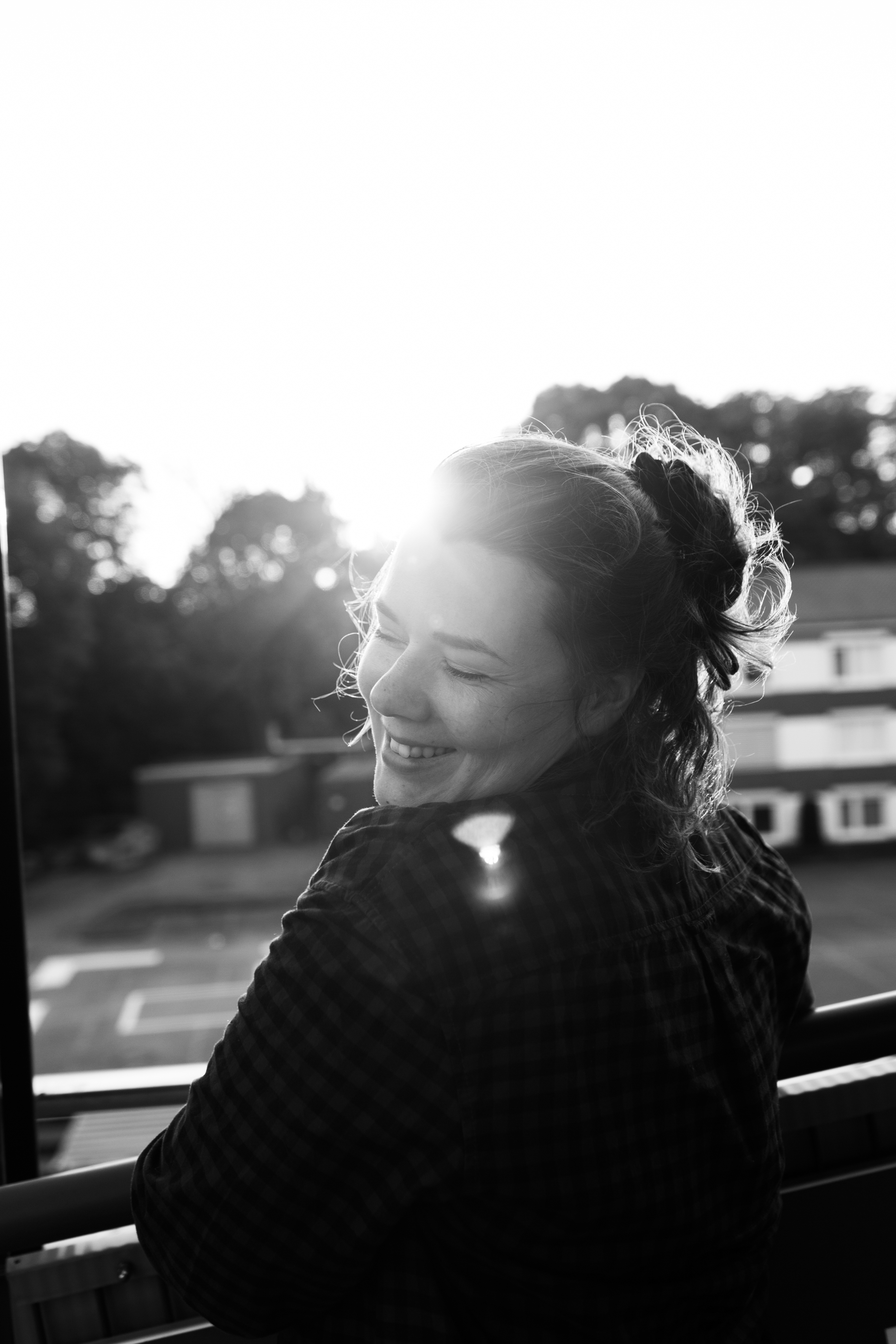 Black and white photo of a woman smiling and looking over her shoulder with sunlight behind her.
