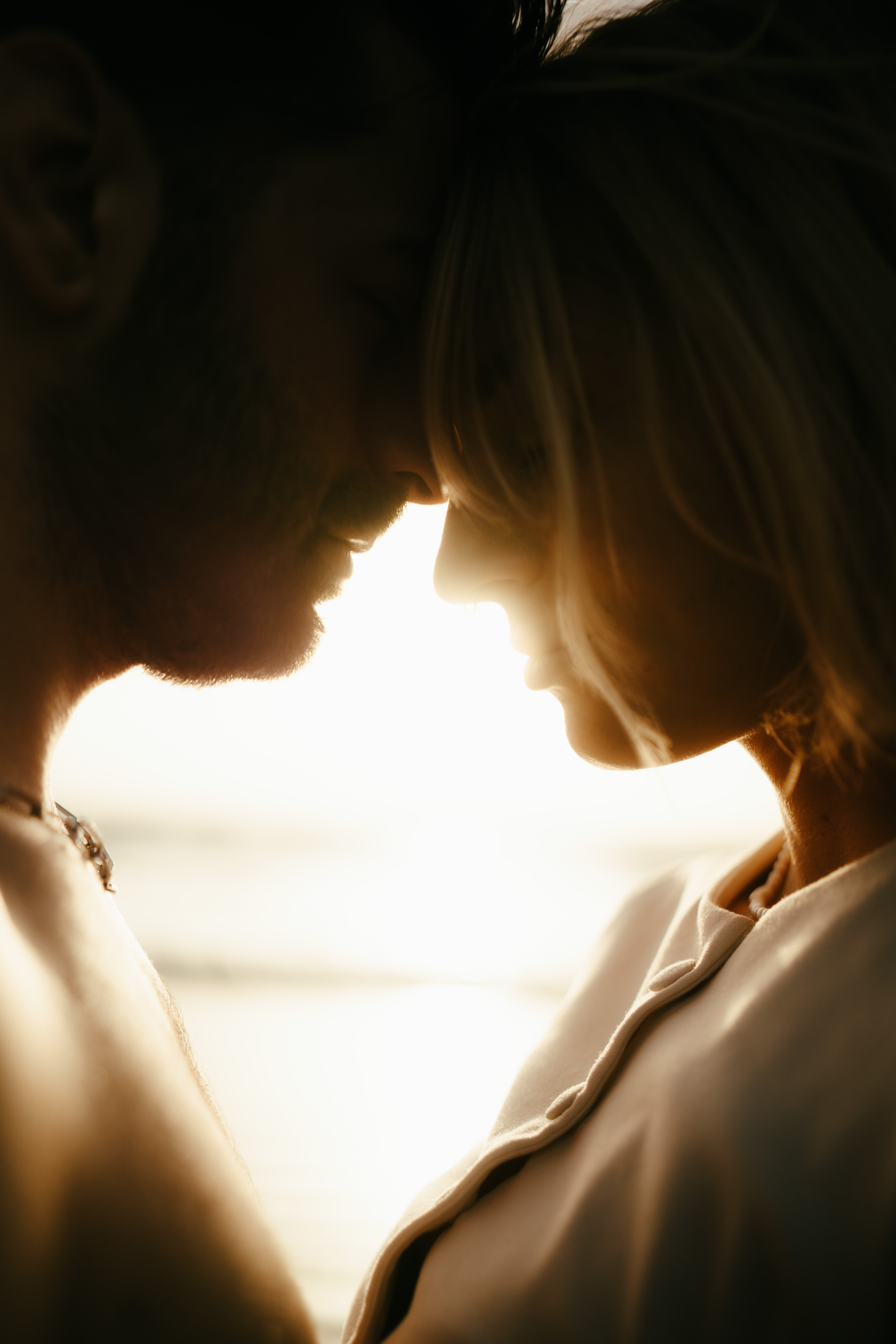 Silhouetted close-up of a man and woman touching foreheads with soft sunlight behind them.