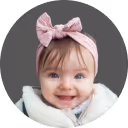Smiling baby girl with blue eyes wearing a pink bow headband and a white outfit.