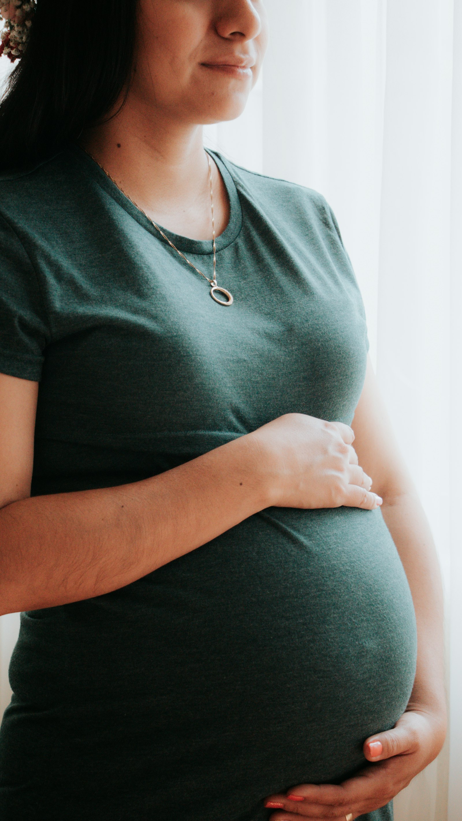 Schwangere Frau im T-Shirt haelt ihren Babybauch
