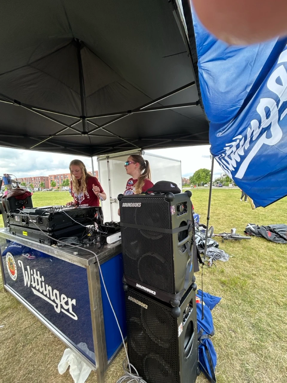 Zwei Frauen legen an einem DJ-Stand unter einem Pavillon auf, daneben gestapelte SOUNDBOKS Lautsprecher.