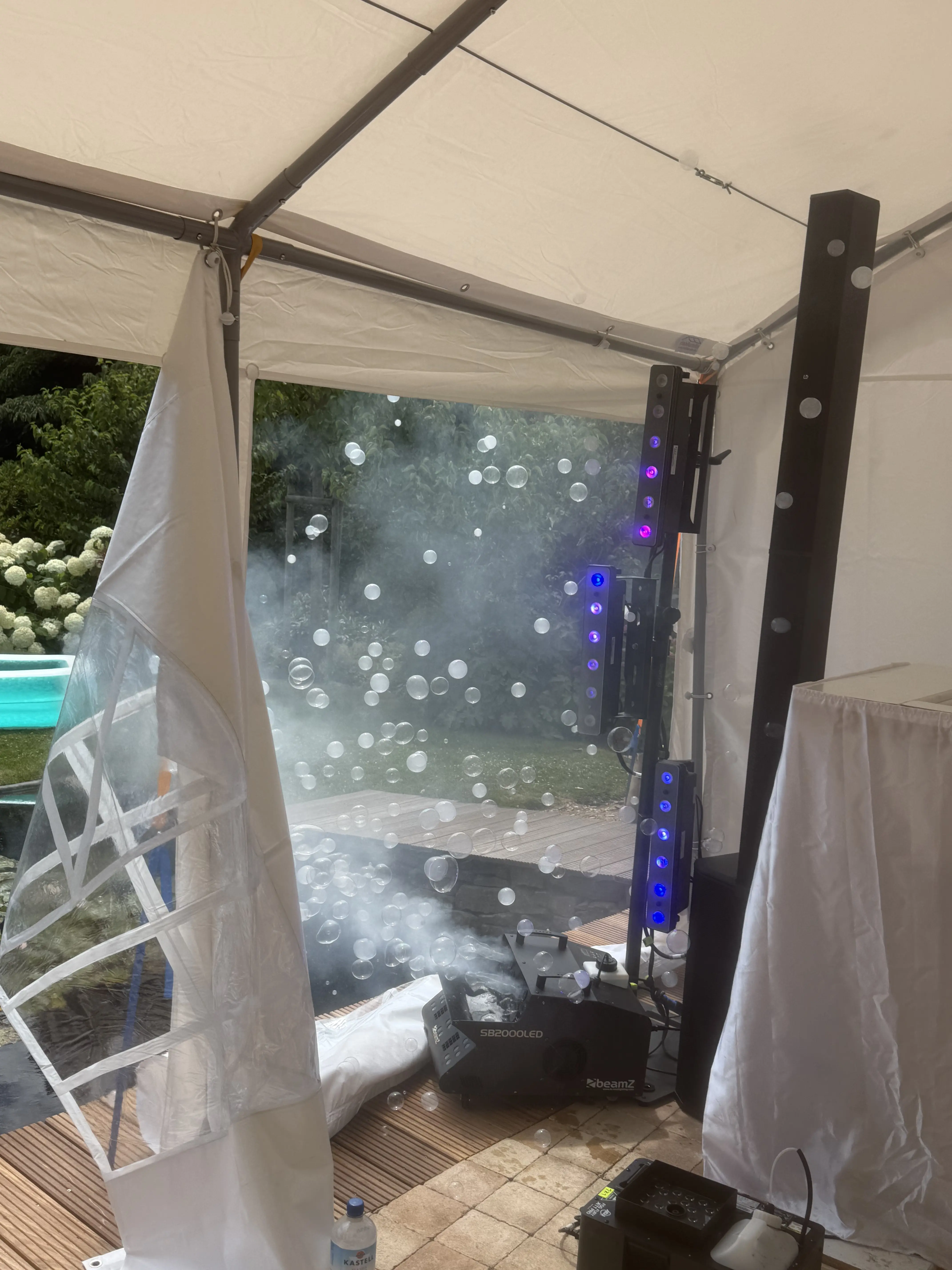 Nebel und Seifenblasen vor einem Partyzelt mit violett leuchtenden LED-Lichtleisten bei einer Gartenparty.