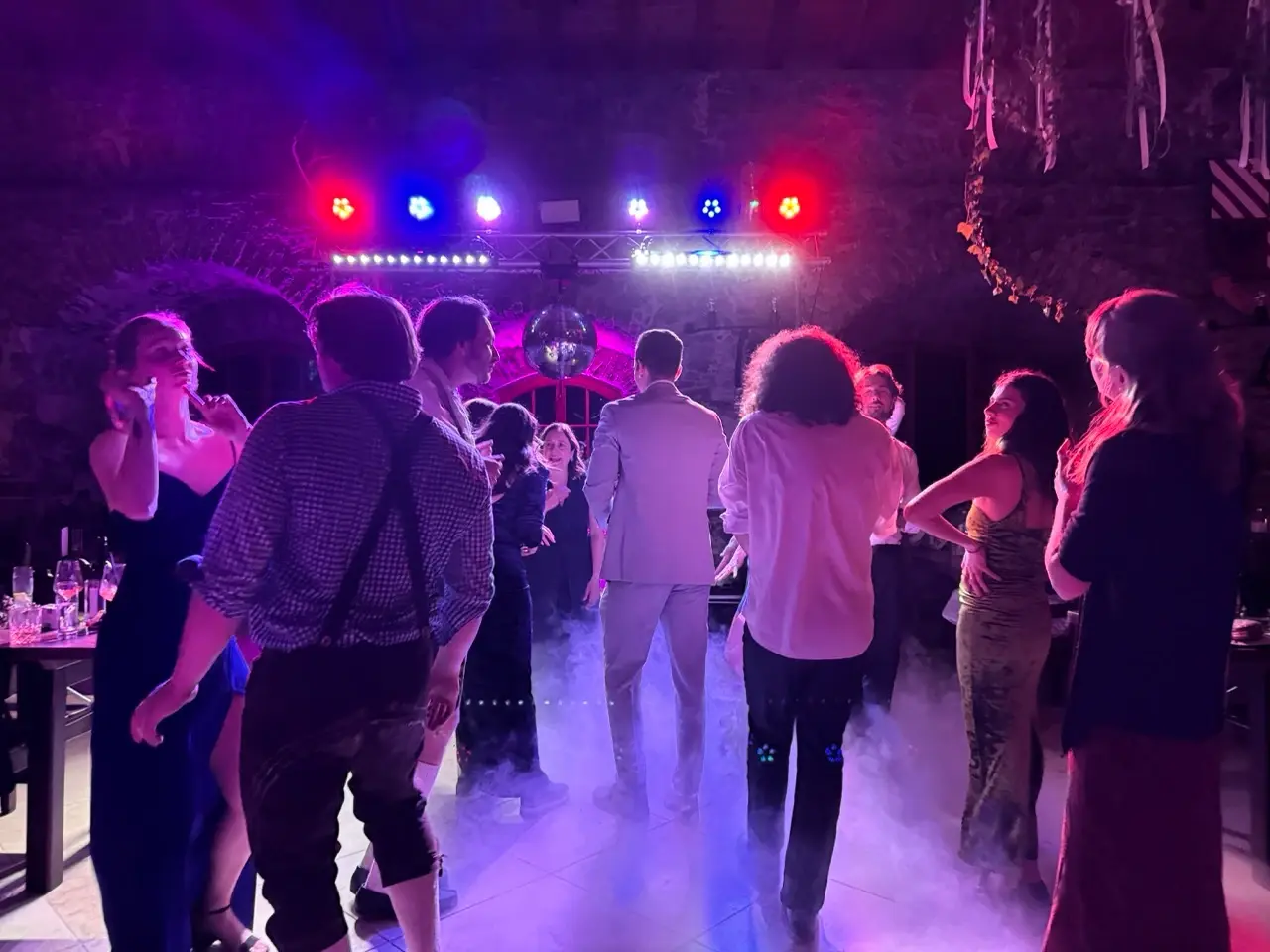 Menschen tanzen in einem Club mit bunten Lichtern und Nebel auf dem Boden.