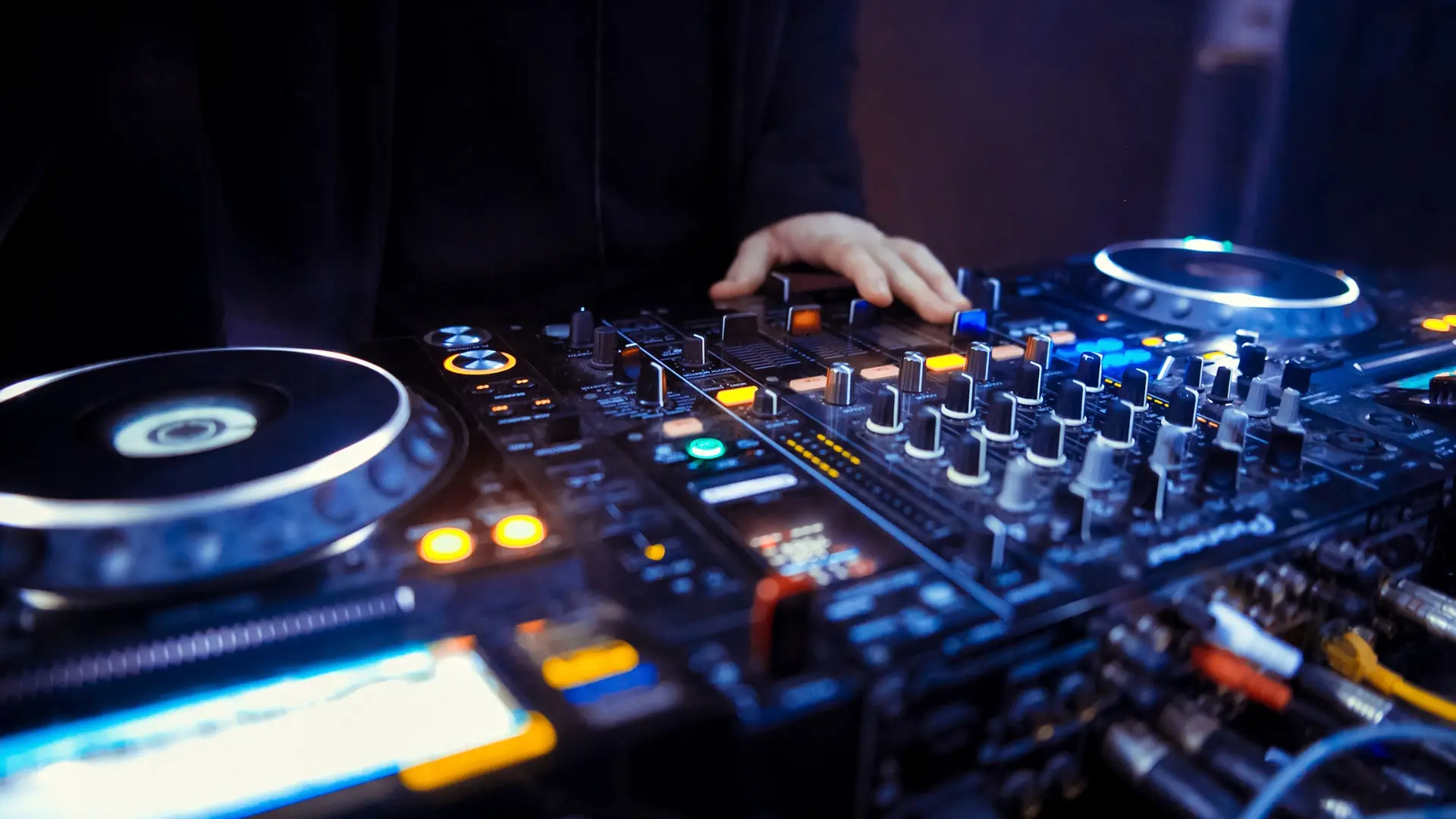 DJ-Mischpult mit Drehreglern, beleuchteten Tasten und einem Hand, die einen Regler bedient.