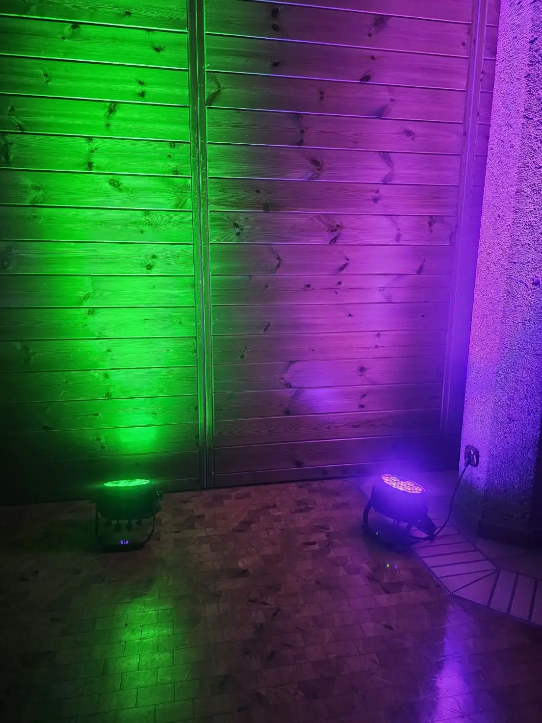 Zwei Bodenstrahler werfen grünes und violettes Licht auf eine Holztür und den Boden.