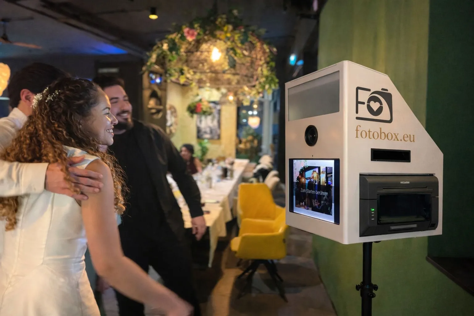 Brautpaar und Gäste haben Spaß bei der Bedienung der Renty Fotobox mit Touchscreen während einer Hochzeitsfeier im Restaurant.
