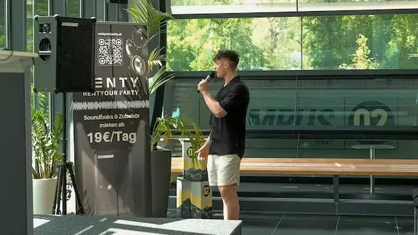 Ein Gast singt mit Funkmikrofon auf einem Event, daneben ein Lautsprecher auf Stativ