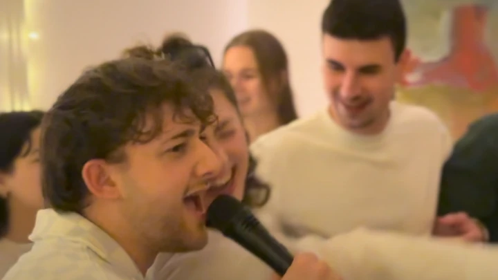 Geburtstagsgäste singen gemeinsam Karaoke, vorne ein junger Mann mit Mikrofon