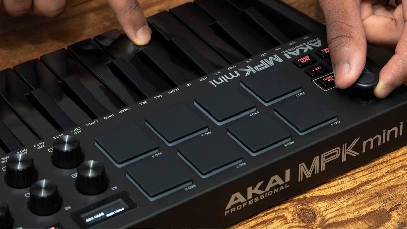 Akai MPK Mini MIDI-Keyboard in Schwarz, Nahaufnahme der Drum-Pads beim Spielen auf einem Holztisch.