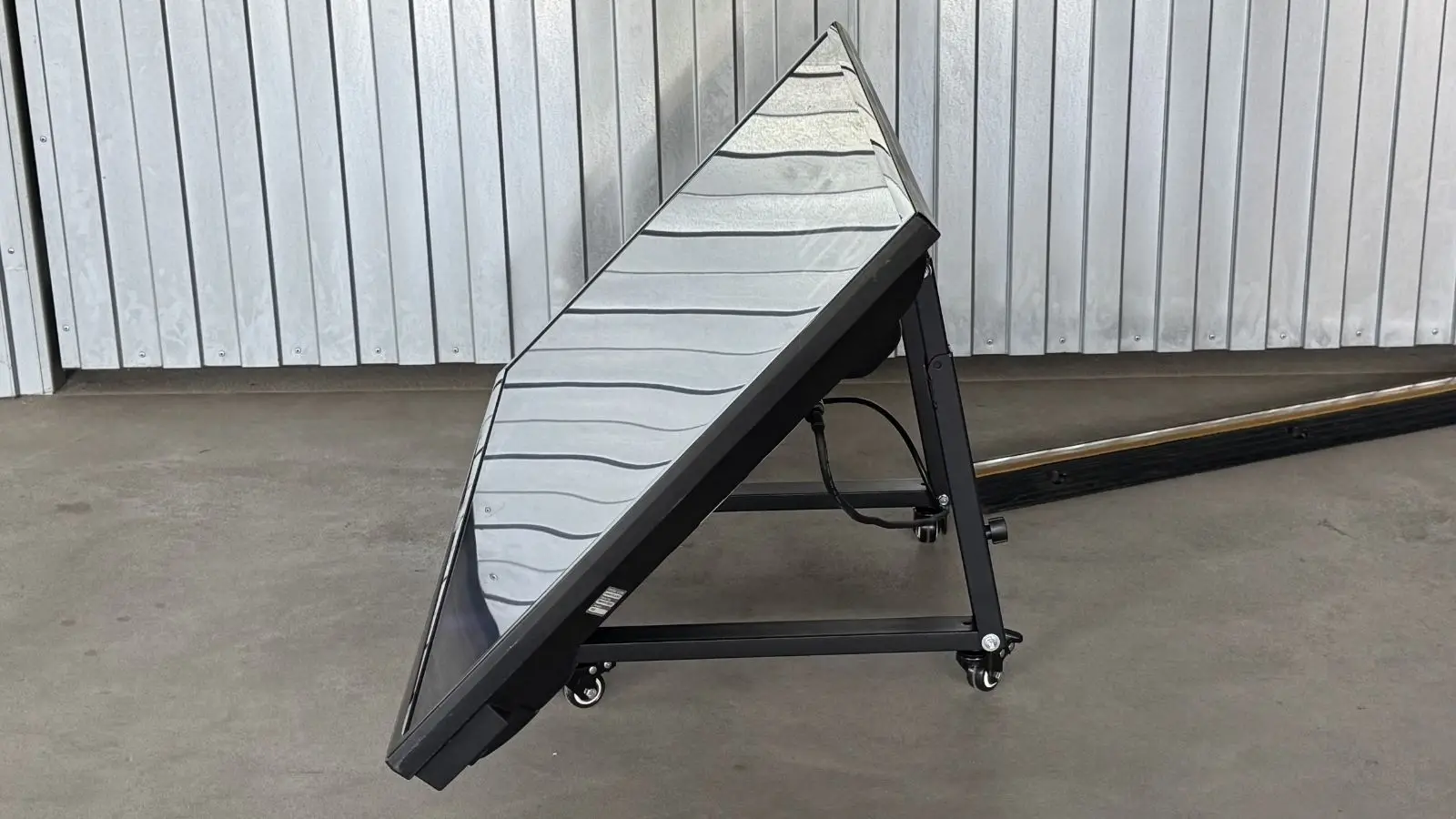 48 Zoll Vorschaumonitor in Seitenansicht auf rollbarem Klappständer mit sichtbarer Rückseite vor Metallwand.