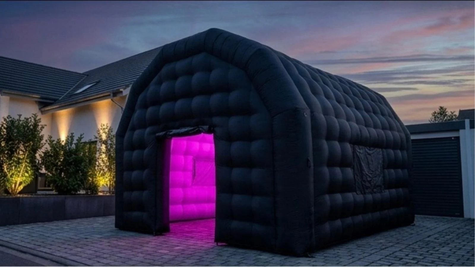 Schwarzes aufblasbares Partyzelt VEVOR mit pink beleuchtetem Eingang in der Abenddämmerung.