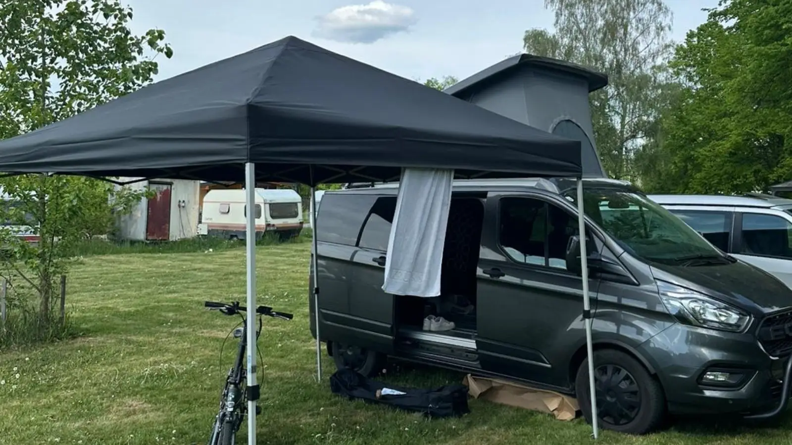 Schwarzer Partyzelt Pavillon 3x3m aufgebaut neben einem Campervan auf einem Campingplatz.
