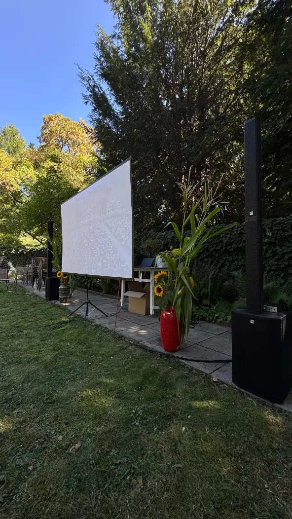 Gartenkino mit Leinwand, Säulenlautsprecher und Subwoofer neben Sonnenblumen als PA-Anlage mieten in Erlangen.