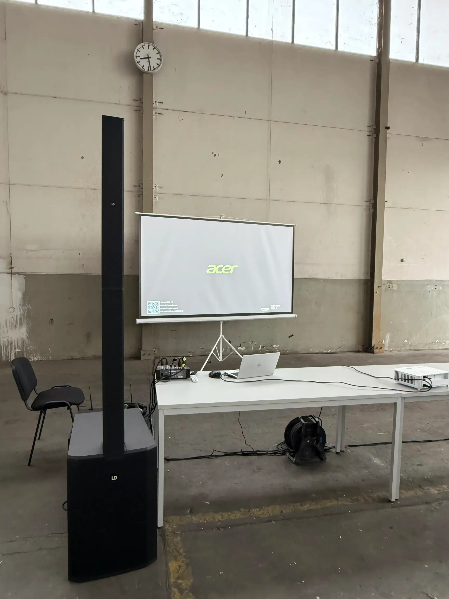 Säulenlautsprecher mit Subwoofer neben Leinwand und Laptop in einer Halle als PA-Anlage mieten in Essen.