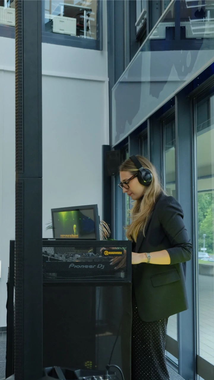 DJ mit Kopfhörern am Pioneer DJ-Pult in einem hellen Foyer, Musikanlage mieten in Hamburg.
