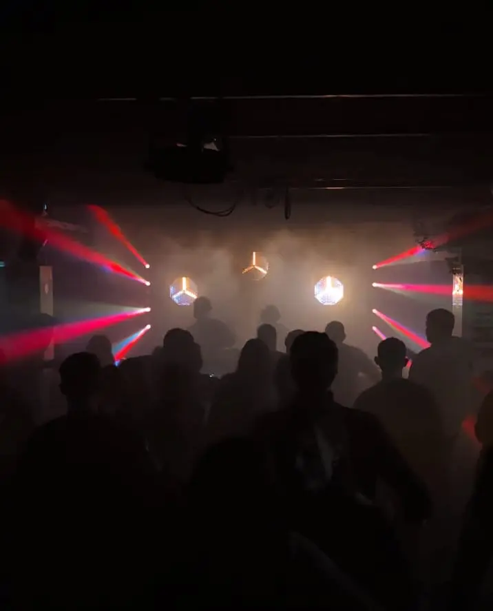 Feiernde Menge mit roten Lichtstrahlen und Nebel in einem dunklen Club als Veranstaltungstechnik mieten in München.