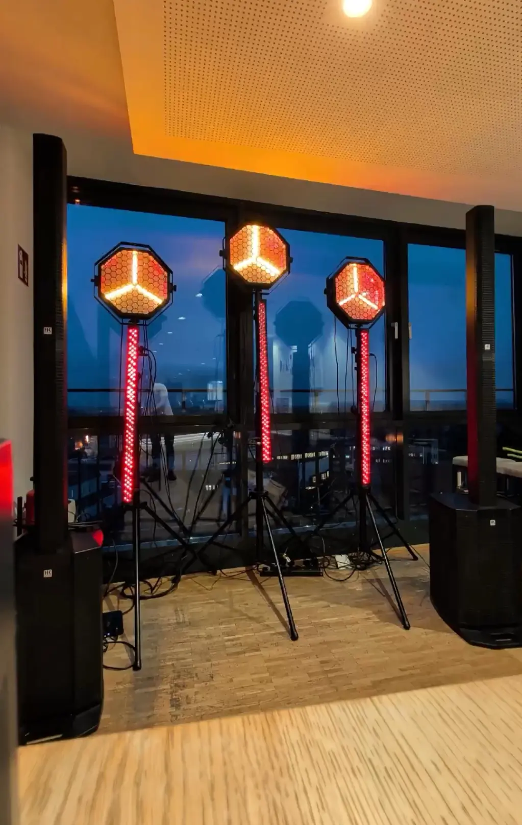Drei Effektstrahler auf Stativen mit roten LED-Leisten und Lautsprechern im Raum für Veranstaltungstechnik mieten in Münster.