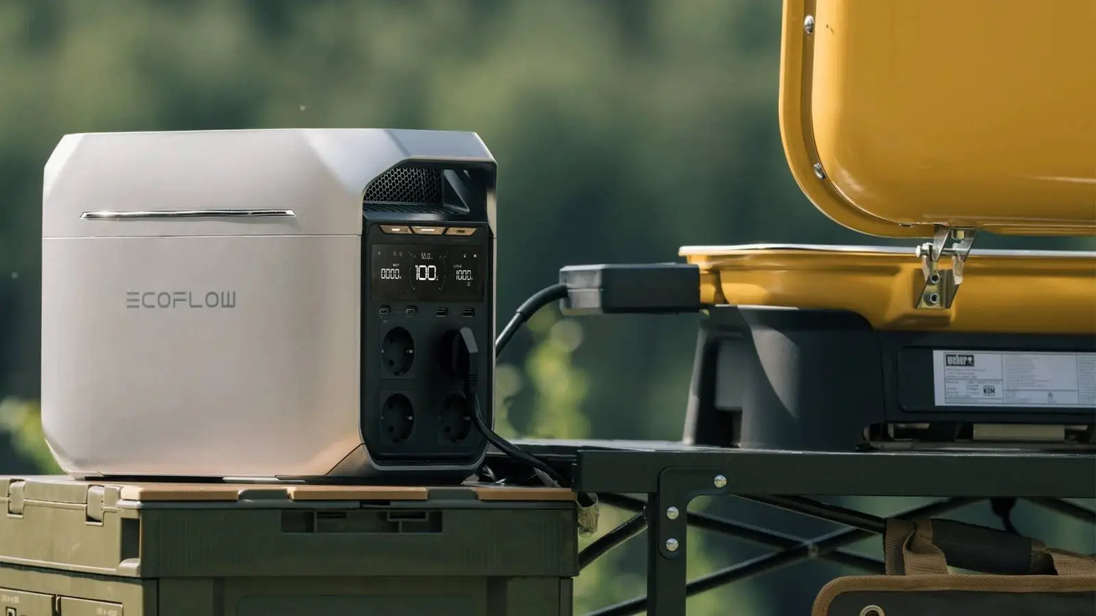 EcoFlow Delta 3 Plus Powerstation in Silbergrau auf einem Campingtisch im Freien neben einer Kühlbox.