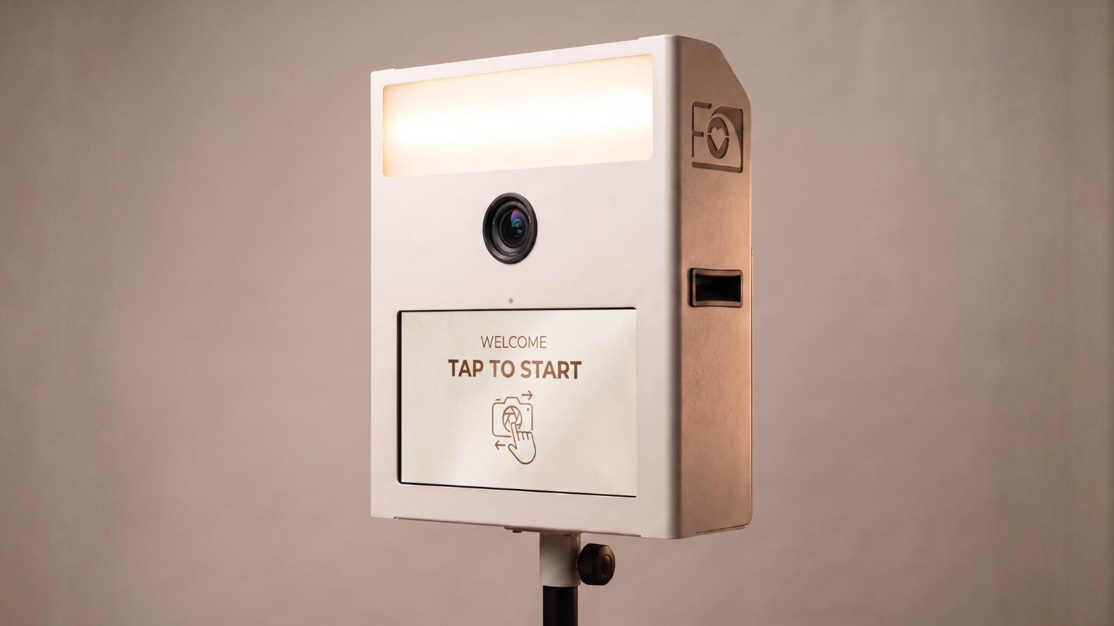 Fotobox Mini in Weiß mit Kamera, Beleuchtung und Touchscreen mit der Aufschrift Tap to Start.