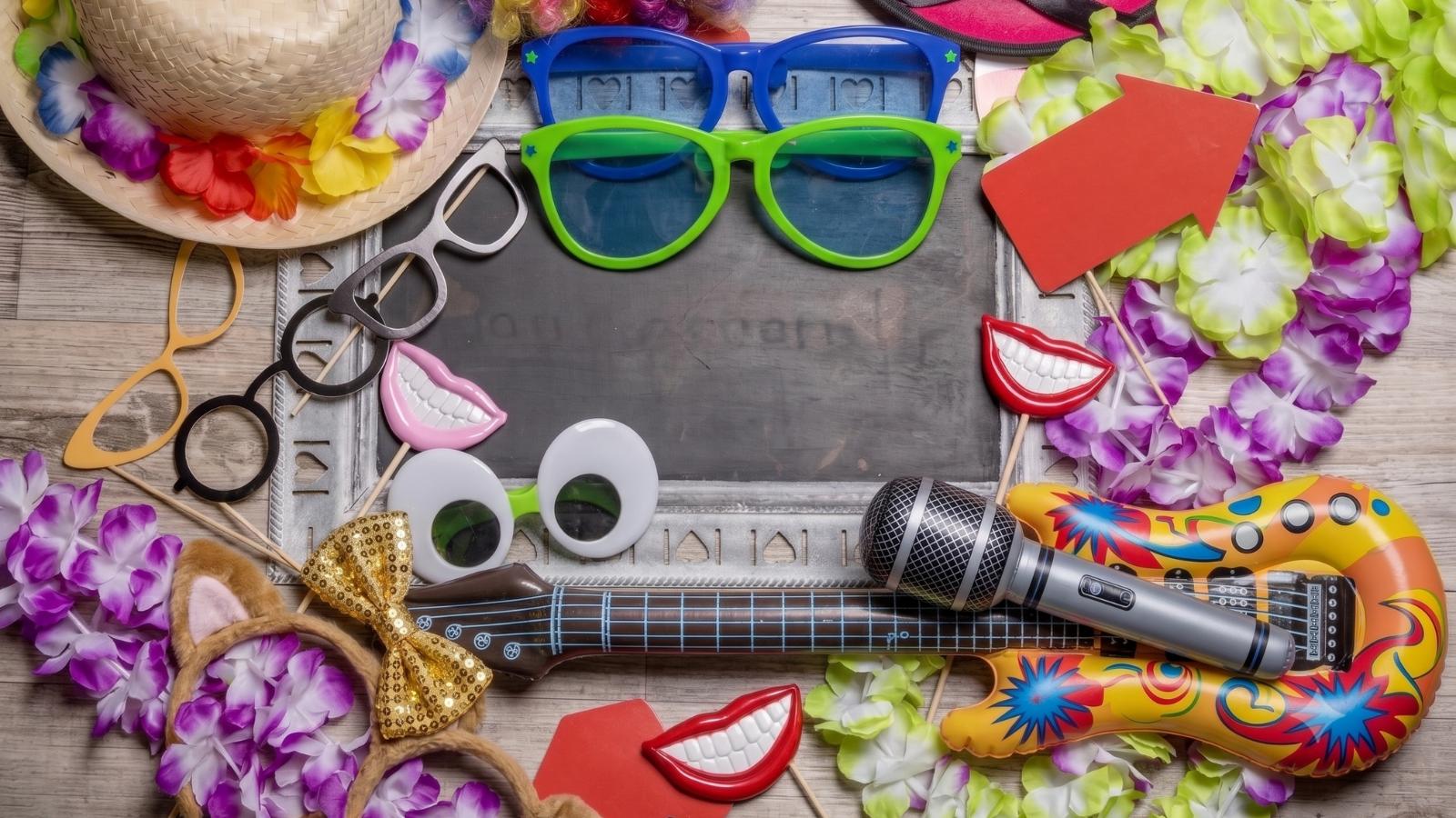 Bunte Fotobox-Requisiten wie Spaßbrillen, Schnurrbärte, Mikrofon und Blumenketten flach angeordnet.