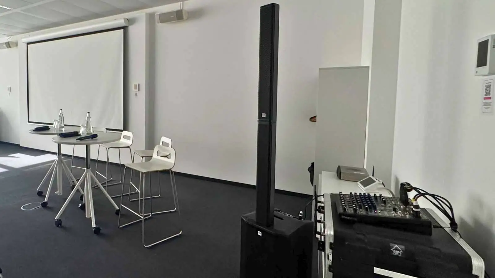 Konferenz Komplettpaket im Seminarraum mit Leinwand, schwarzem Säulenlautsprecher, Mischpult und Stehtisch.
