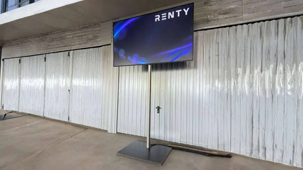 Fernseher auf Standfuß mit Renty-Logo aus dem Konferenz Komplettpaket, aufgestellt vor einer Wand.