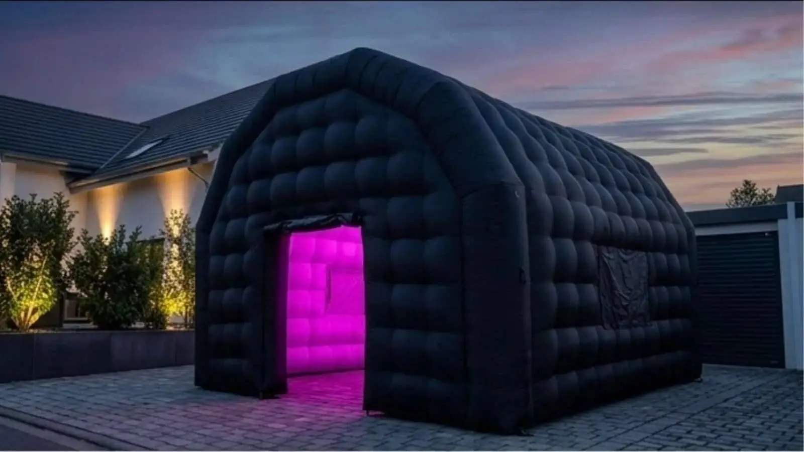 Aufblasbares schwarzes Partyzelt aus dem Outdoor Partyzelt Paket mit pink beleuchtetem Eingang in der Abenddämmerung.