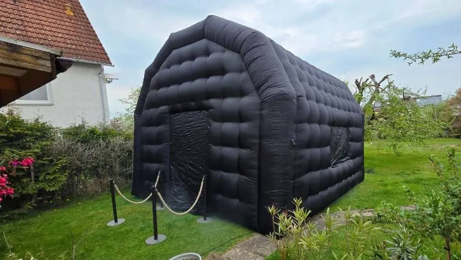 Schwarzes aufblasbares Partyzelt aus dem Outdoor Partyzelt Paket im Garten mit Absperrung bei Tageslicht.