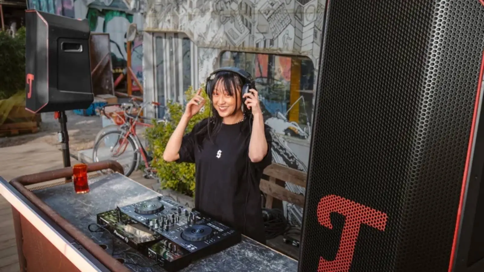 DJ mit Kopfhörern und Controller neben dem Teufel Rockster Air 2 Akku-Lautsprecher bei einer Open-Air-Party.