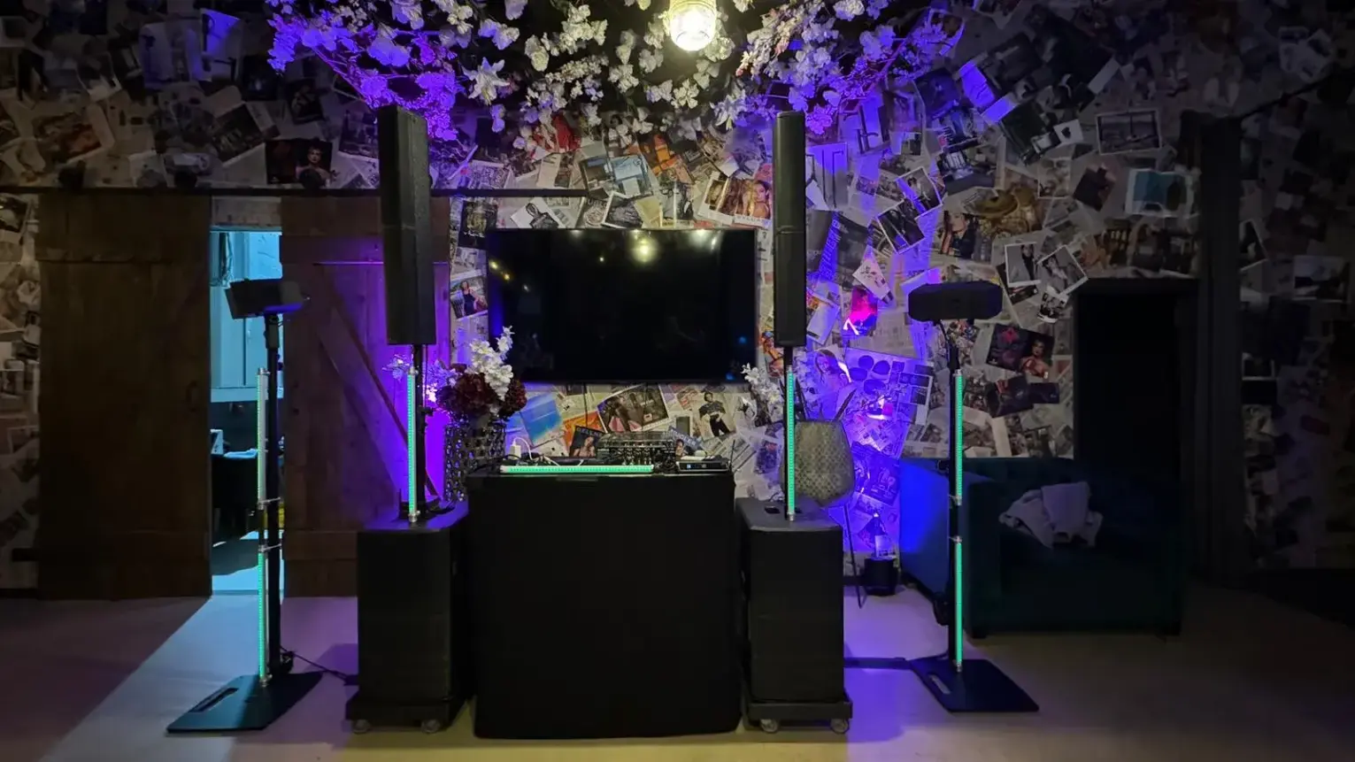 DJ-Pult mit Bildschirm, Lautsprechern und LED-Röhren vor einer Fotowand, PA-Anlage für Weihnachtsfeier mieten.