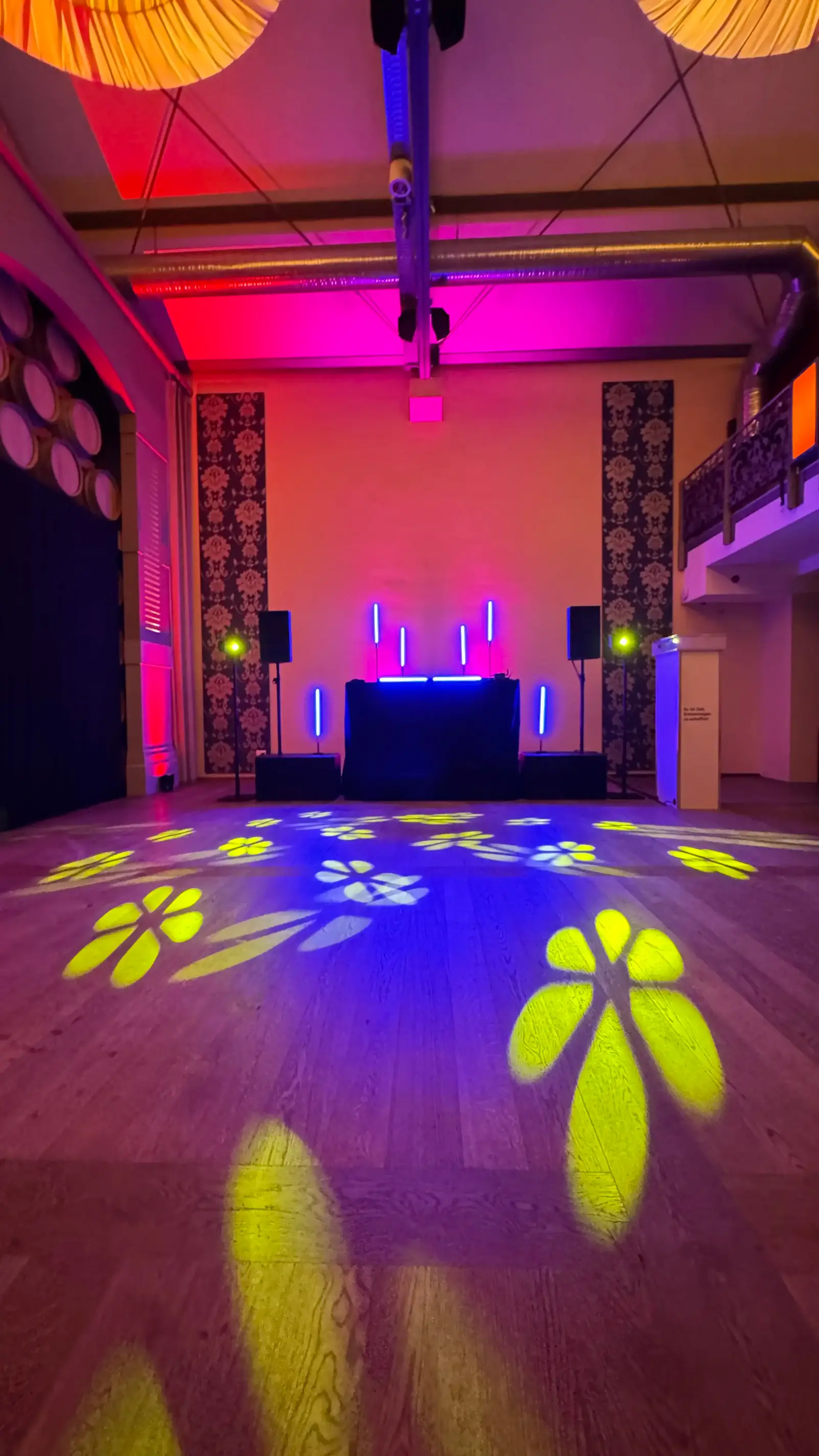 DJ-Aufbau mit Lautsprechern, LED-Röhren und gelben Blumen-Gobos auf dem Boden im Saal, Veranstaltungstechnik für Junggesellenabschied mieten.
