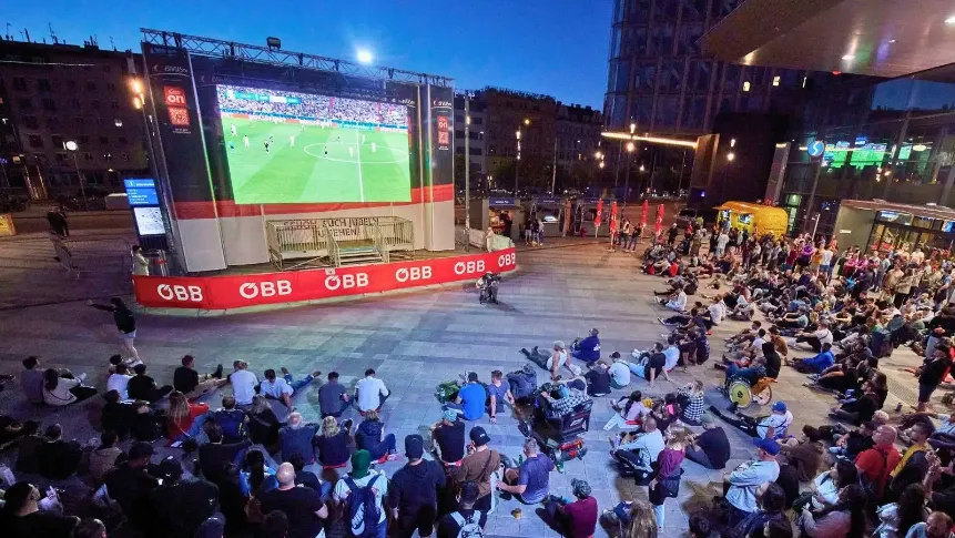 Publikum sitzt abends vor einer großen Videowand mit Fußballspiel auf einem Platz, Veranstaltungstechnik für Public Viewing mieten.