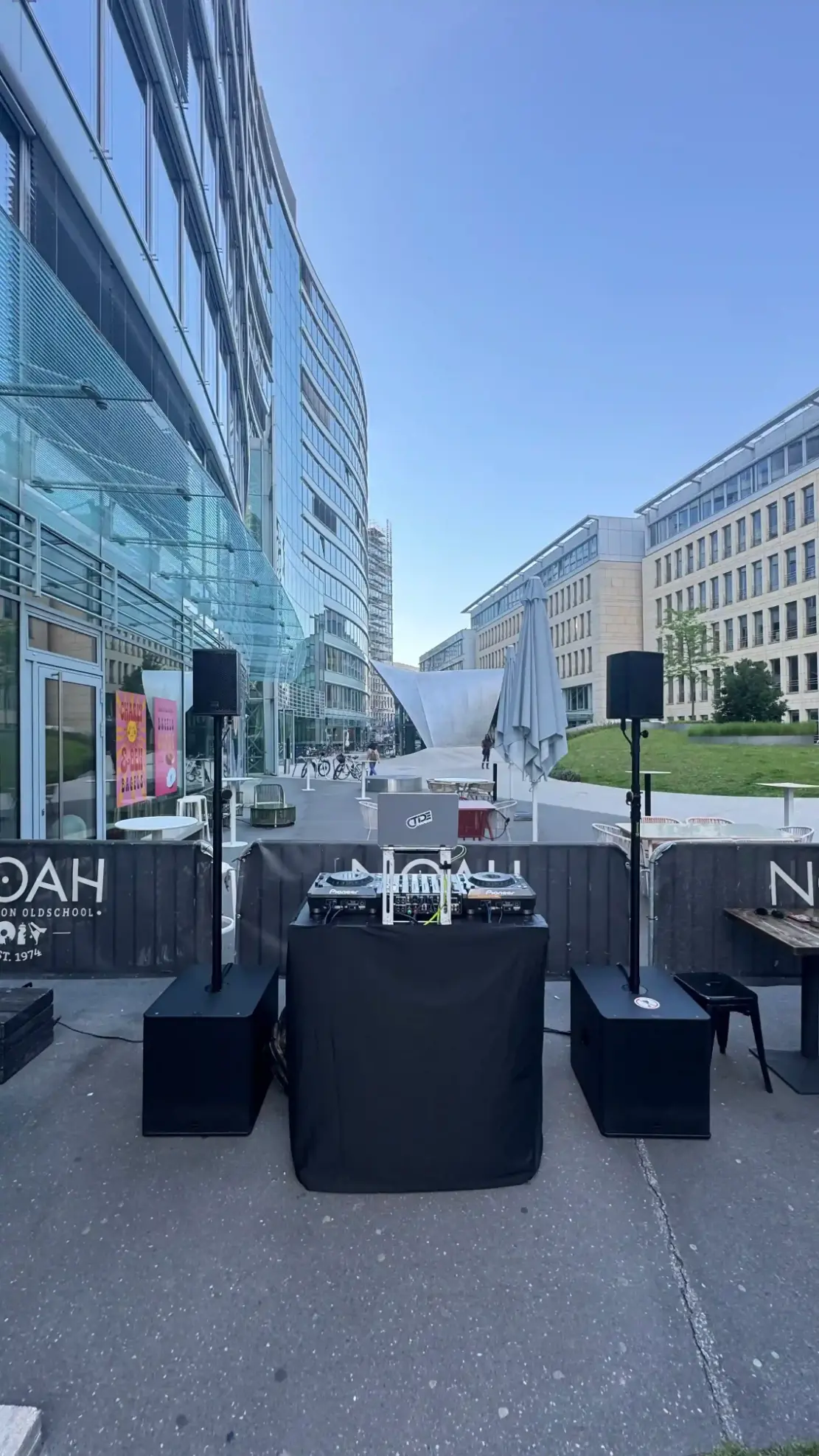 DJ-Pult mit zwei Lautsprechern auf Stativen vor Bürogebäuden im Freien, PA-Anlage für Public Viewing mieten.