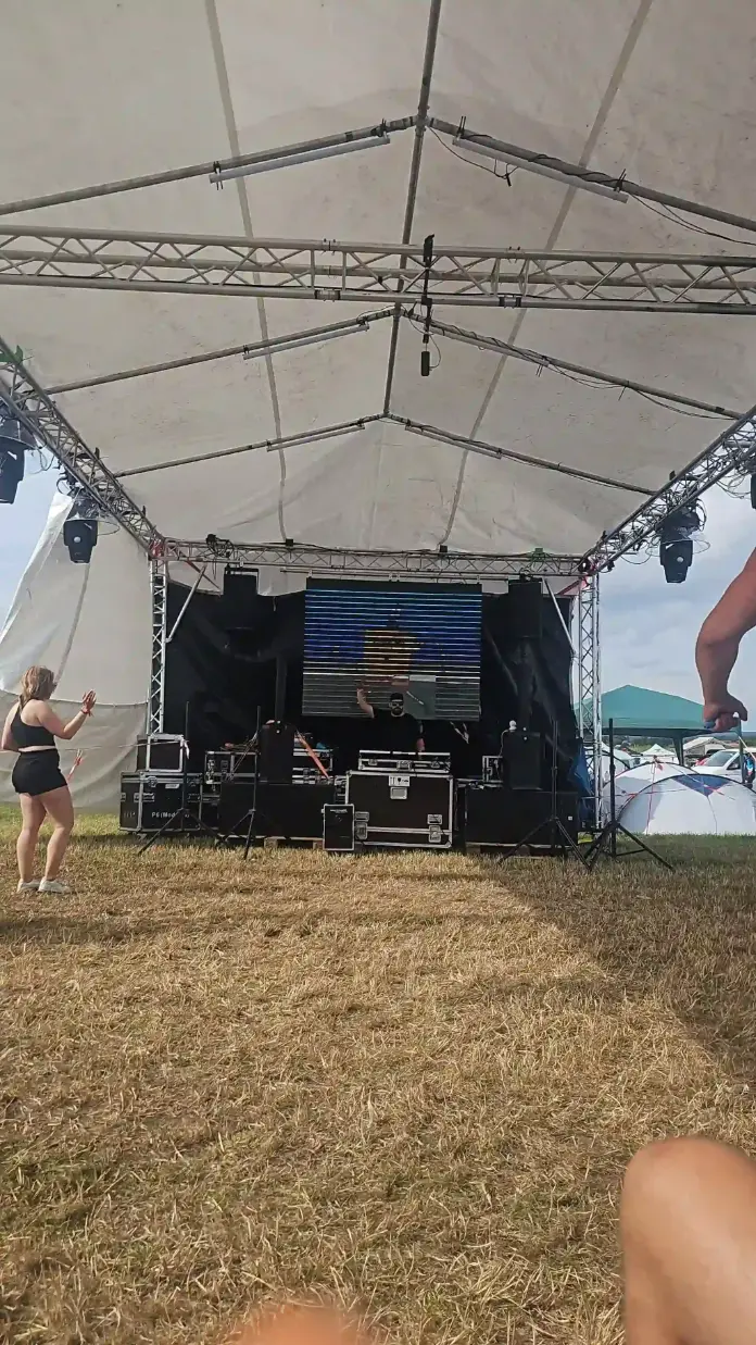 Zeltbühne mit LED-Wand und Lautsprechern auf einer Wiese mit tanzender Person, Veranstaltungstechnik für Public Viewing mieten.